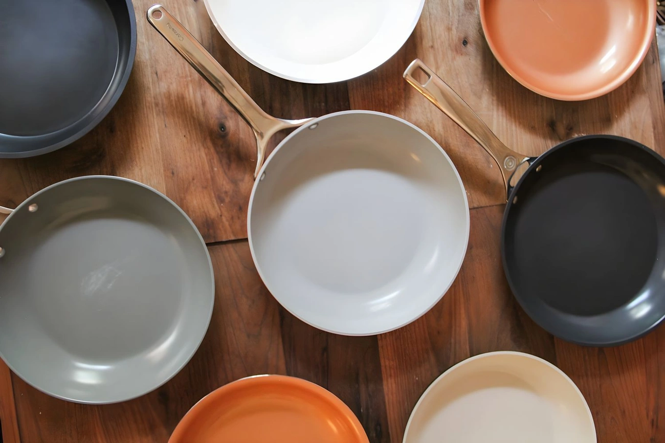 Najlepsze patelnie – Przewodnik Kupującego + Ranking Top 5 Top view of various ceramic nonstick frying pans in different colors arranged on a wooden surface.