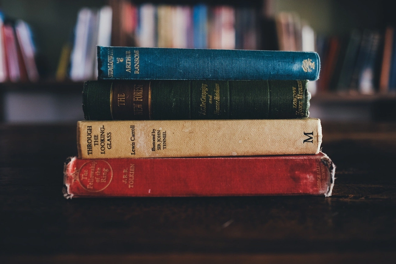 Najlepsze książki 2025 roku, które musisz przeczytać Stack of vintage classic books including works by J.R.R. Tolkien, Lewis Carroll, and Arthur Ransome on a wooden table.