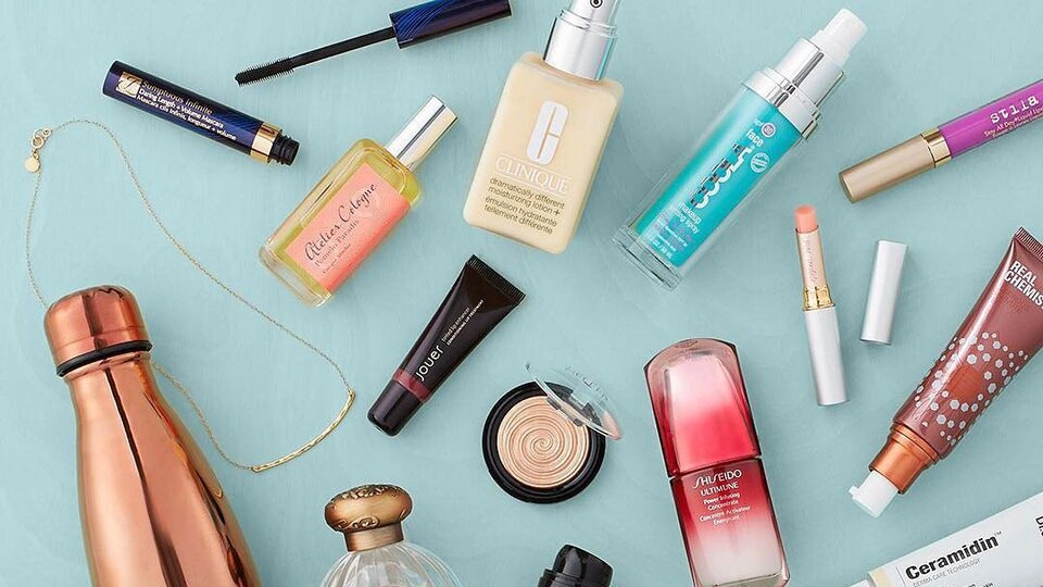 Top10 - Najlepsze Podkłady do Twarzy: Co Ukrywają Profesjonaliści? Flat lay of various beauty products and accessories on a light blue background, including foundation, perfume, and lipstick.
