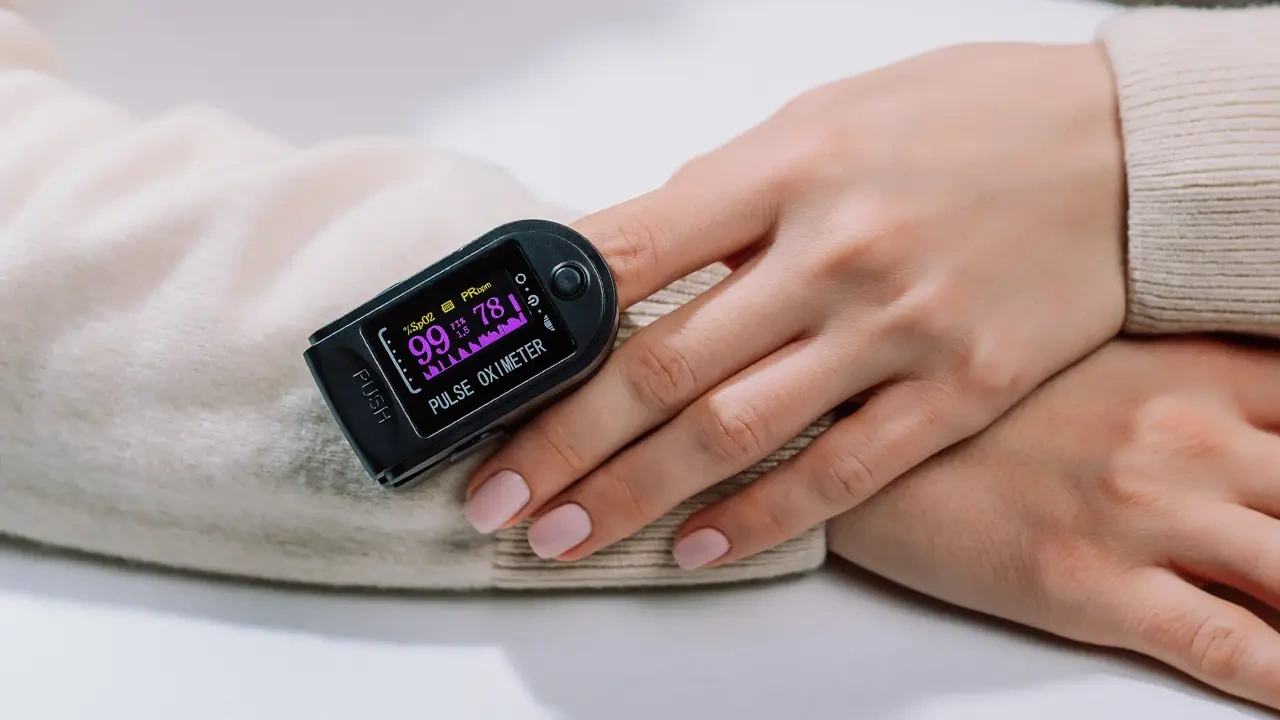 Person using a pulse oximeter clipped on their finger to measure blood oxygen saturation and pulse rate.