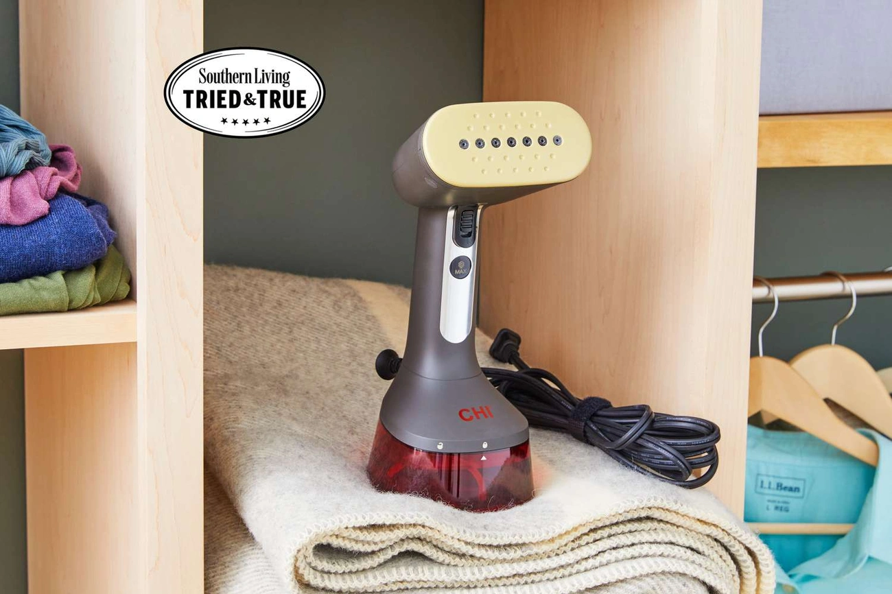 Najlepsze Parownice do Ubrań w 2025 - Prosty Przewodnik Zakupowy CHI handheld clothing steamer placed on a folded wool sweater inside a wooden closet with folded clothes and hangers nearby.