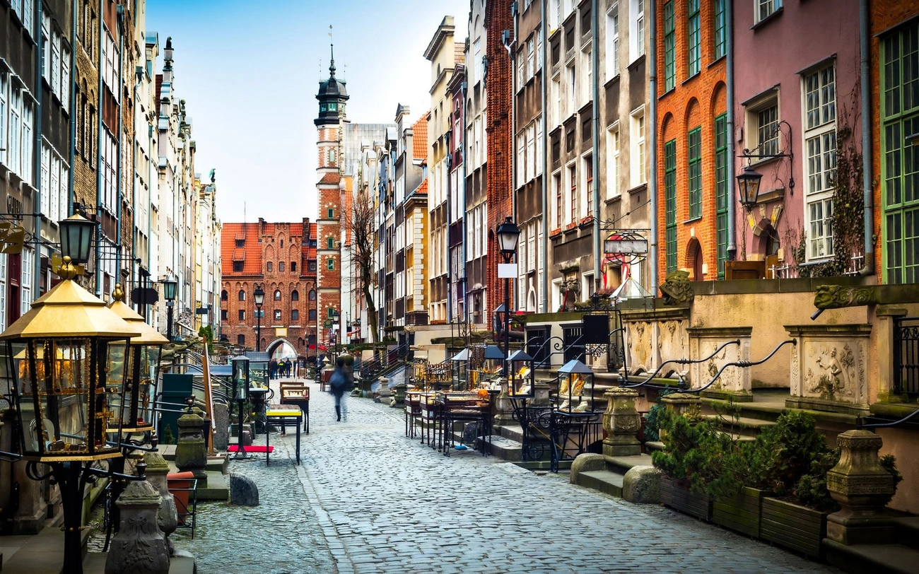 Cobblestone street in a historic Polish city lined with colorful buildings and outdoor cafes under a clear sky.