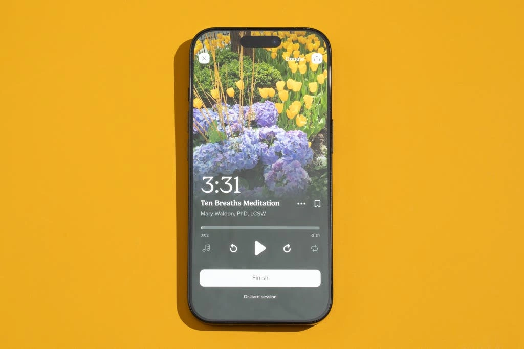 Aplikacje Do Medytacji Dla Zabieganych: Jak Znalazłam 10 Minut Spokoju? Smartphone displaying a meditation app with a floral background and a 3:31 timer on a yellow surface.
