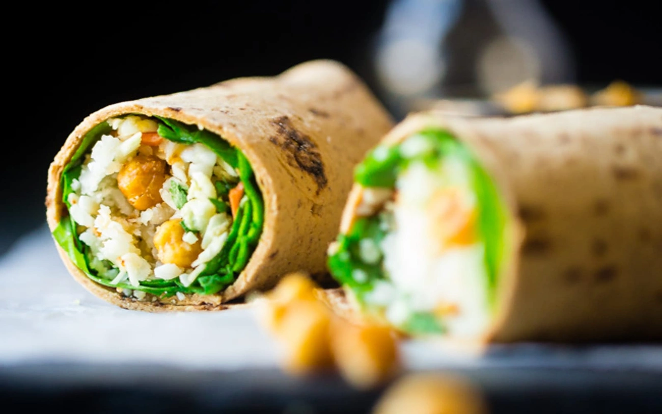 Jak Zrobić Domowe Przekąski Bezglutenowe w 15 Minut Close-up of a vegan and gluten-free wrap filled with chickpeas, rice, spinach, and vegetables on a dark background.