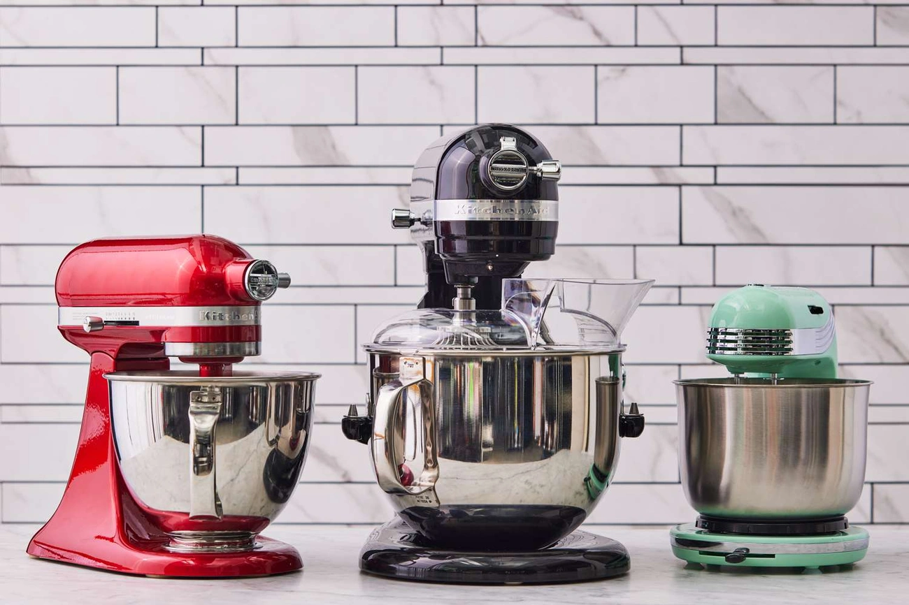 Jak Wybrać Najlepszy Robot Planetarny? Ranking Top 10 + Przewodnik Three stand mixers in red, black, and mint green colors displayed on a kitchen counter with a tiled backsplash.