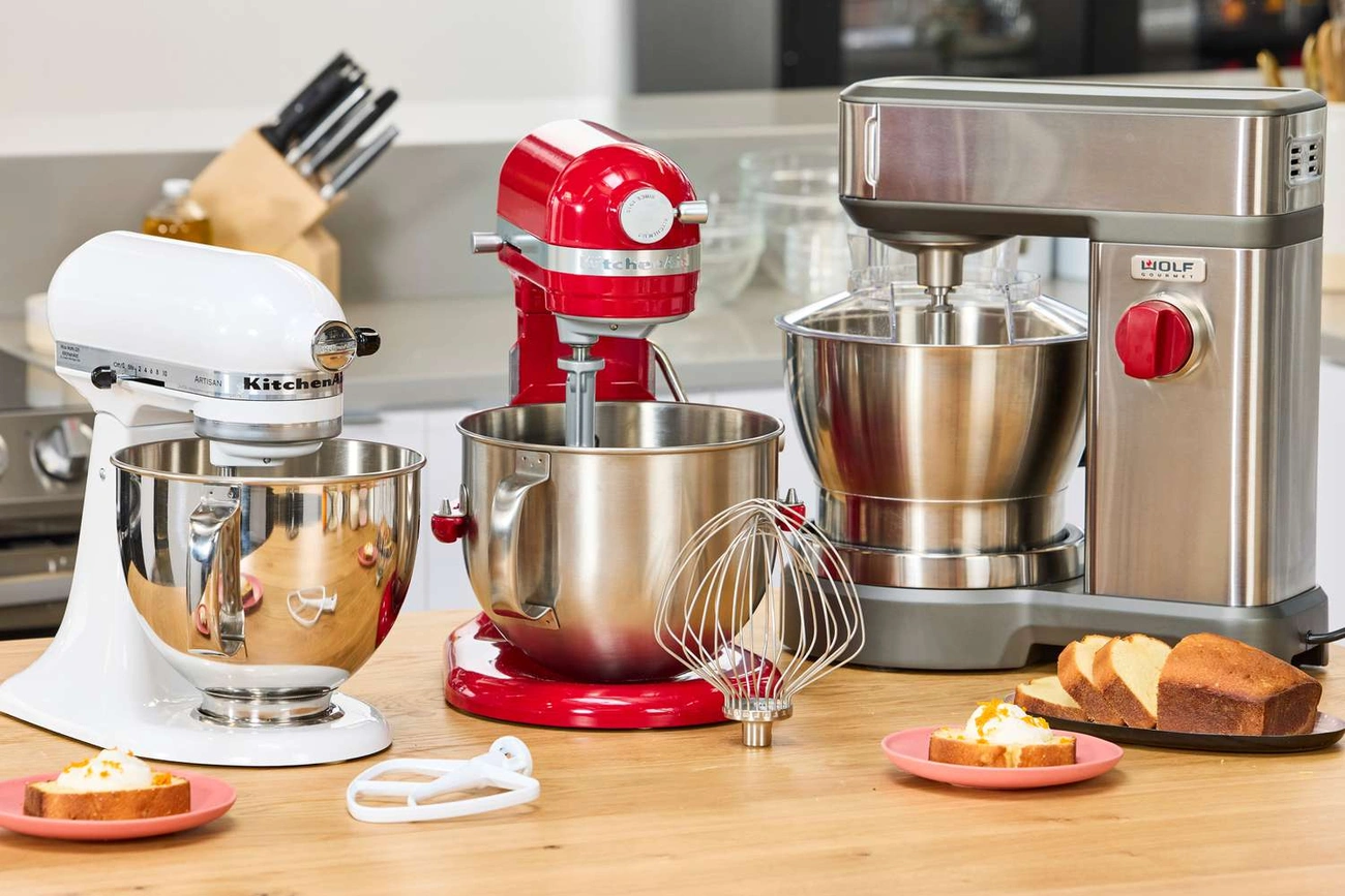 Jak Wybrać Najlepszy Robot Planetarny? Ranking Top 10 + Przewodnik Three stand mixers in white, red, and stainless steel displayed on a kitchen countertop with baked goods nearby.