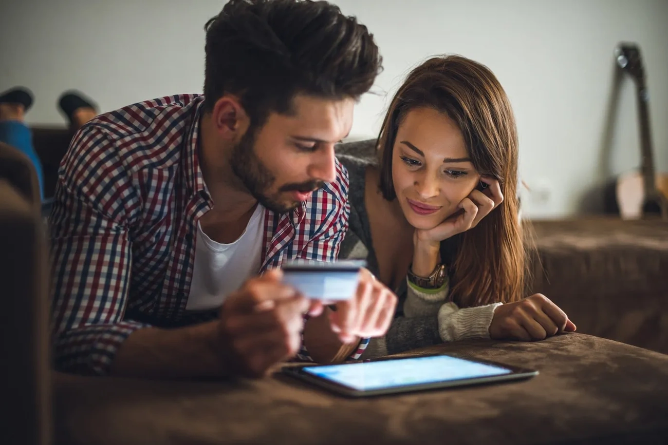 Trejdi Opinie: Uwaga na Oszustwo – 5 Faktów, Które Poznałam Couple lying on a couch using a tablet and holding a credit card for online shopping.