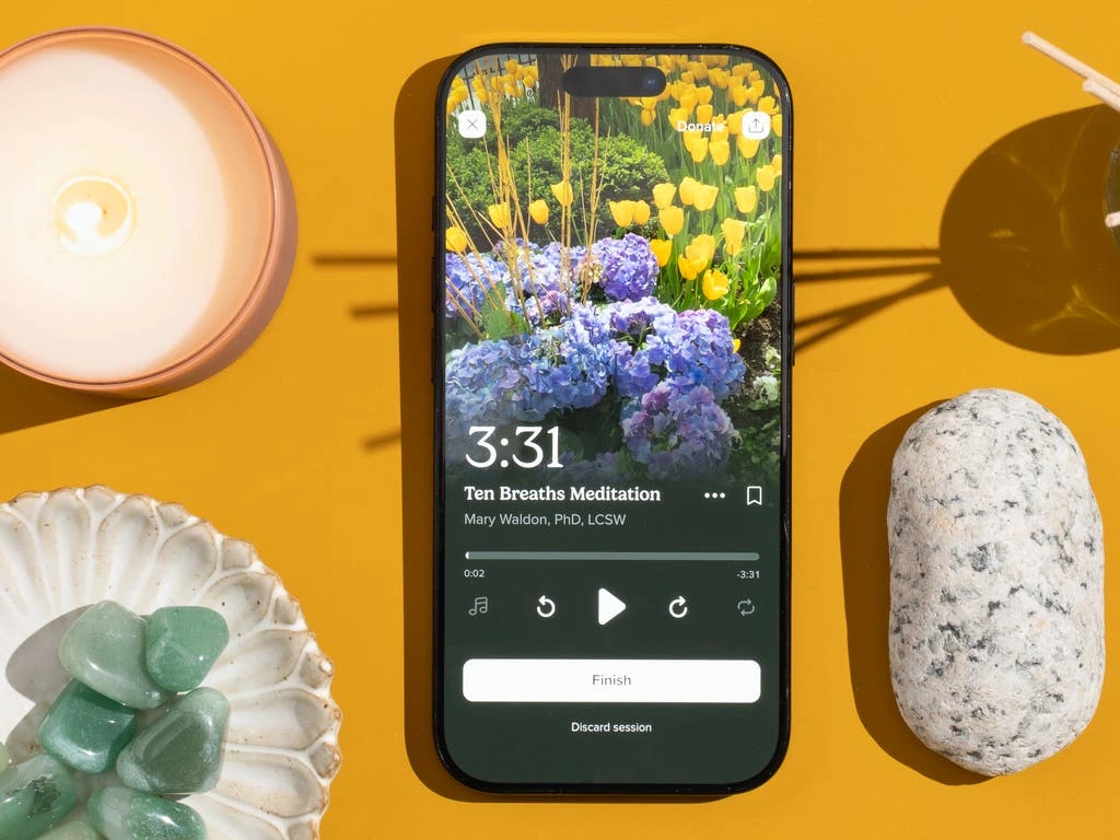 Aplikacje Do Medytacji Dla Zabieganych: Jak Znalazłam 10 Minut Spokoju? Smartphone displaying a Ten Breaths Meditation app session with crystals, a candle, and a stone on a yellow surface.