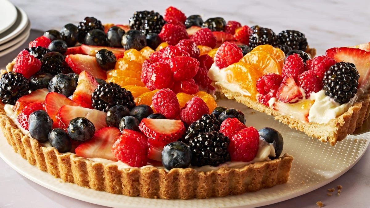 Jak Zrobić Pyszne Desery Bez Cukru? 5 Pomysłów Colorful fruit tart with strawberries, blueberries, raspberries, blackberries, and mandarin orange slices on a plate.