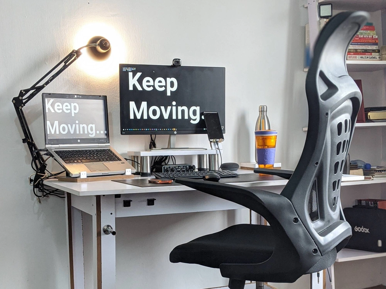 Jak Urządzić Domowe Biuro Do Pracy Zdalnej: Sprawdzone Metody Na 2025 Ergonomic home office setup with dual screens displaying 'Keep Moving' and a supportive black office chair.