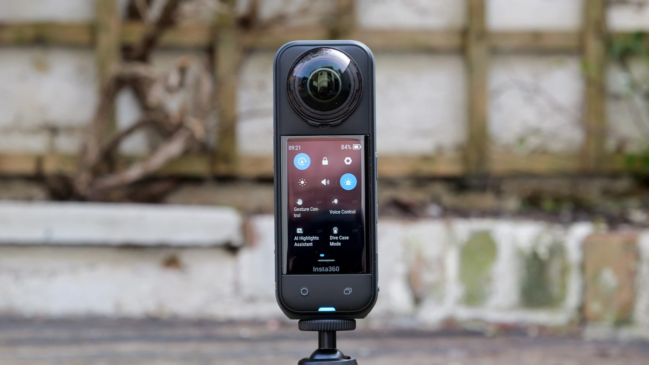 Insta360 360-degree camera with touchscreen displaying settings, mounted on a small tripod outdoors.