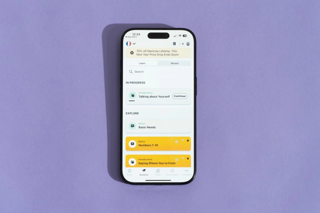 Najlepsze aplikacje do nauki języków obcych w 2025 roku Smartphone displaying a language learning app interface with lessons on basic needs and introductions on a purple background.