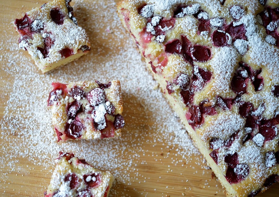 Polish summer fruit cake topped with powdered sugar and cut into squares on a wooden board.