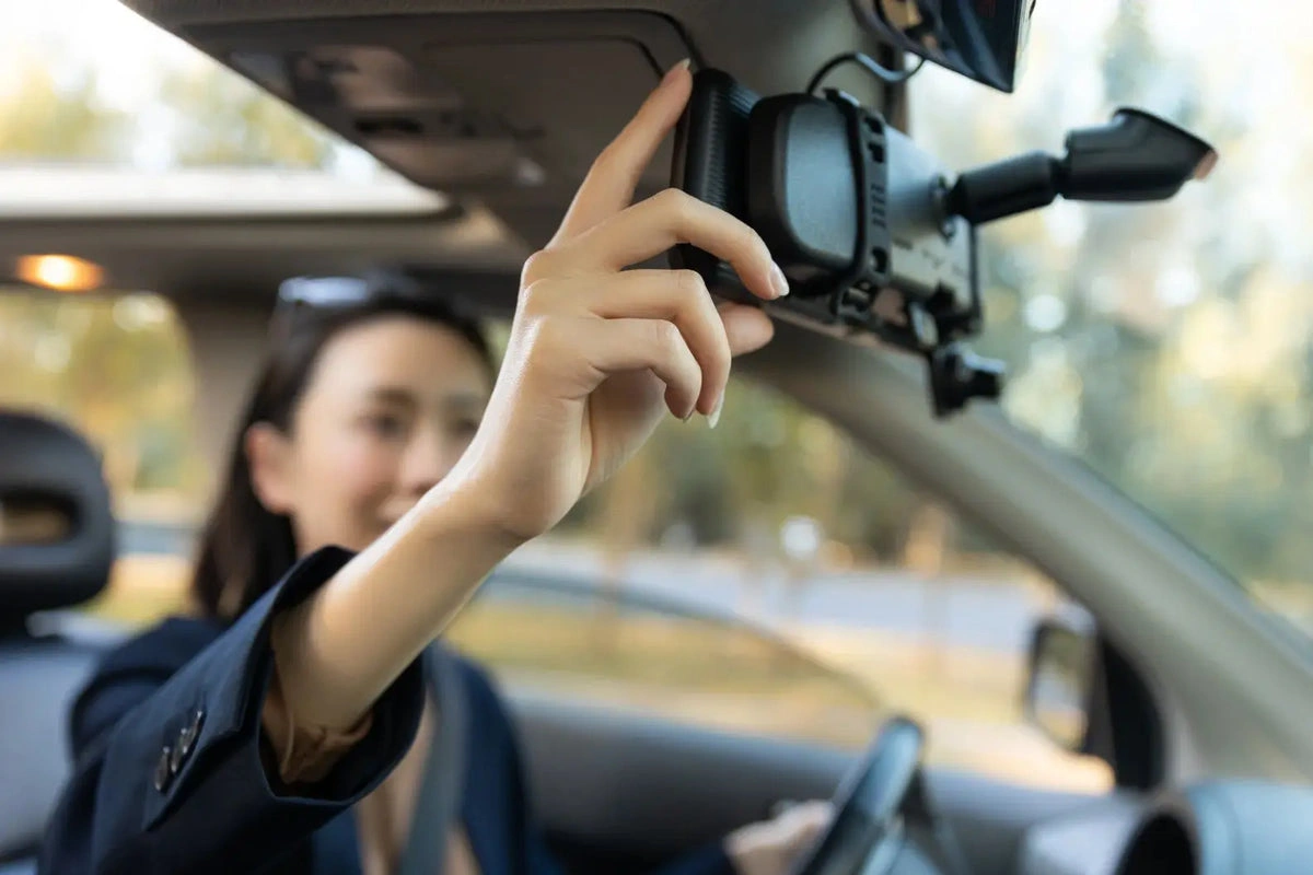 Ranking Kamer Samochodowych — Tanie, Średnia Półka i Premium Osoba montująca kamerę samochodową z trybem parkingowym na przedniej szybie auta w ciągu dnia.