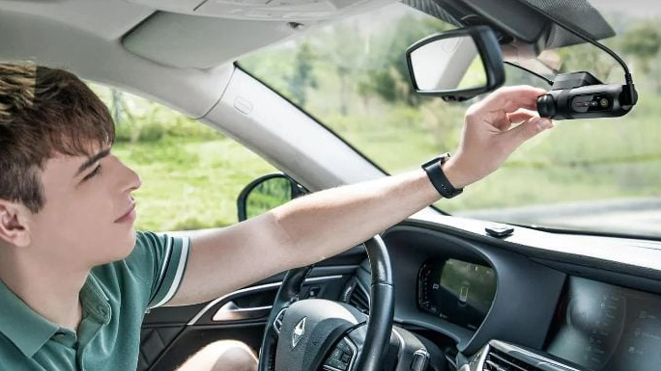Ranking Kamer Samochodowych — Tanie, Średnia Półka i Premium Osoba montująca czarną, trzykanałową kamerę samochodową na przedniej szybie auta, na tle zielonego otoczenia.