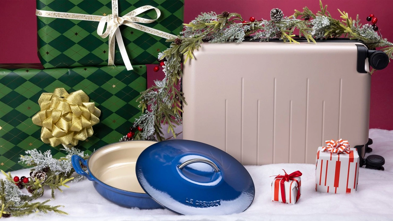 Prezent na Święta 2025: Co Naprawdę Chcą Dostać Twoi Bliscy? !Christmas gift ideas including a blue Le Creuset pan, wrapped presents, and a silver suitcase with festive decorations.