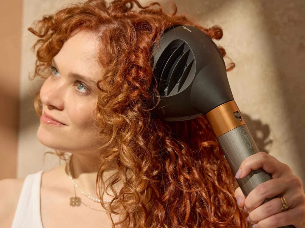 Osoba suszy bujne, kręcone rude włosy za pomocą czarno-miedzianego dyfuzora na neutralnym tle.