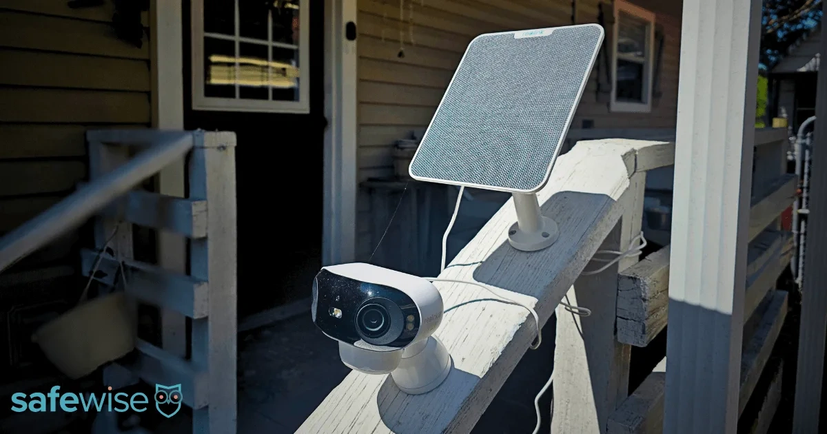 Ranking Kamer Zewnętrznych 2026: Zanim Wydasz Złotówkę, Przeczytaj To Outdoor security camera and solar panel mounted on a white wooden porch railing in daylight, with SafeWise logo.