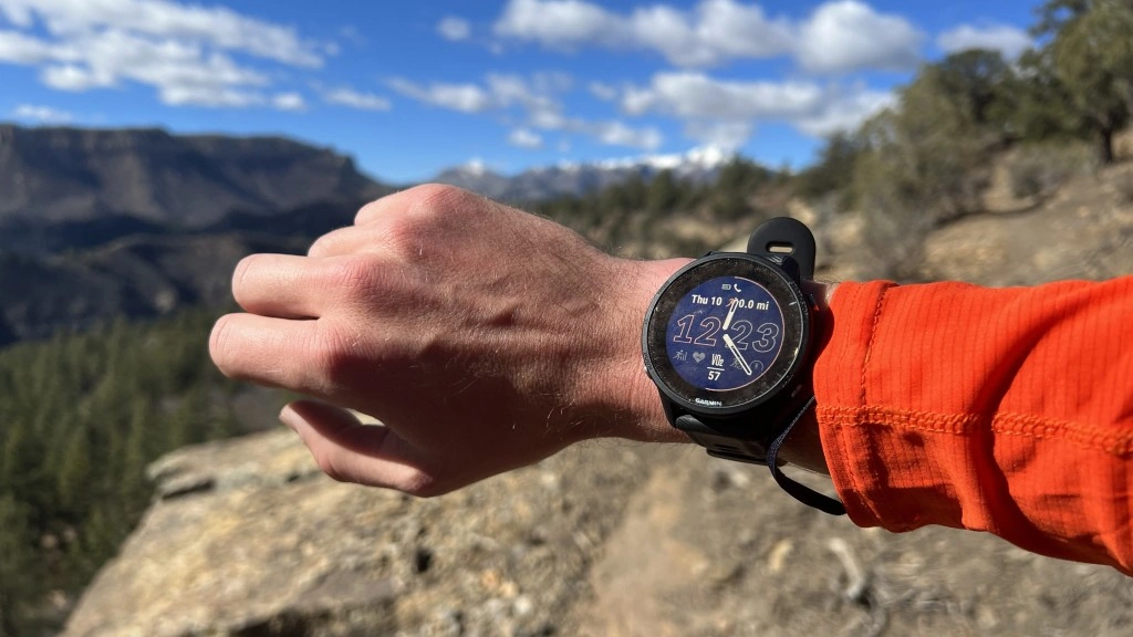 Smartwatch Męski Ranking 2025 | Odkryj 10 Najlepszych! Close-up of a Garmin Forerunner 955 smartwatch on a wrist with a mountain trail background during a sunny day.