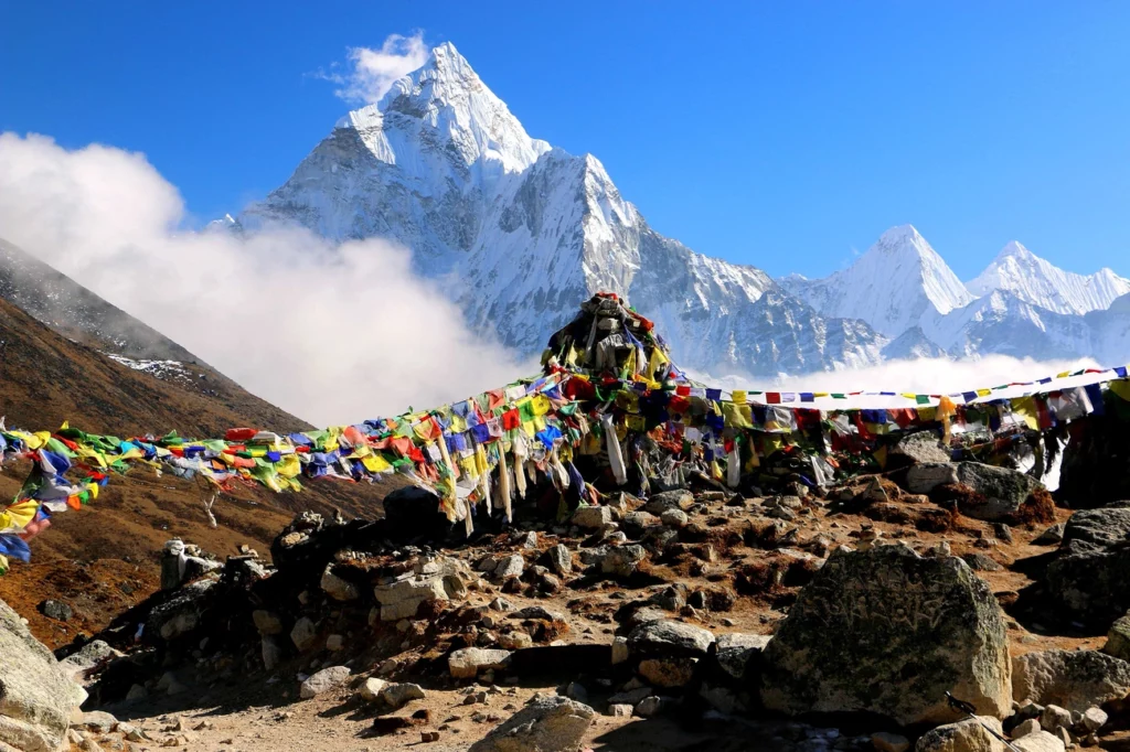 Najlepsze miejsca na wakacje w 2026 roku Colorful prayer flags flutter over rocky terrain with snow-covered Himalayan peaks under a clear blue sky.